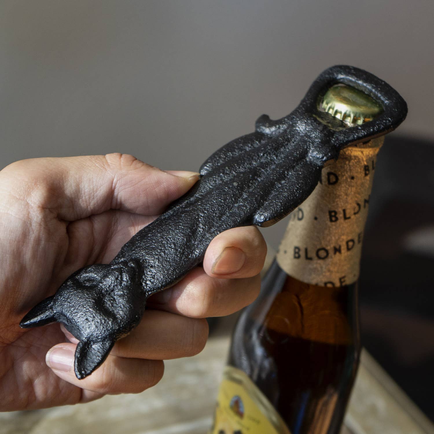 Hand holding a black cast iron bottle opener shaped like a hand, with a bottle in the background.