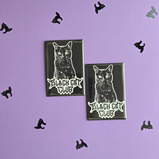 Two black rectangular magnets with a black cat illustration and Black Cat Club logo, displayed on a purple background with small black cat confetti.