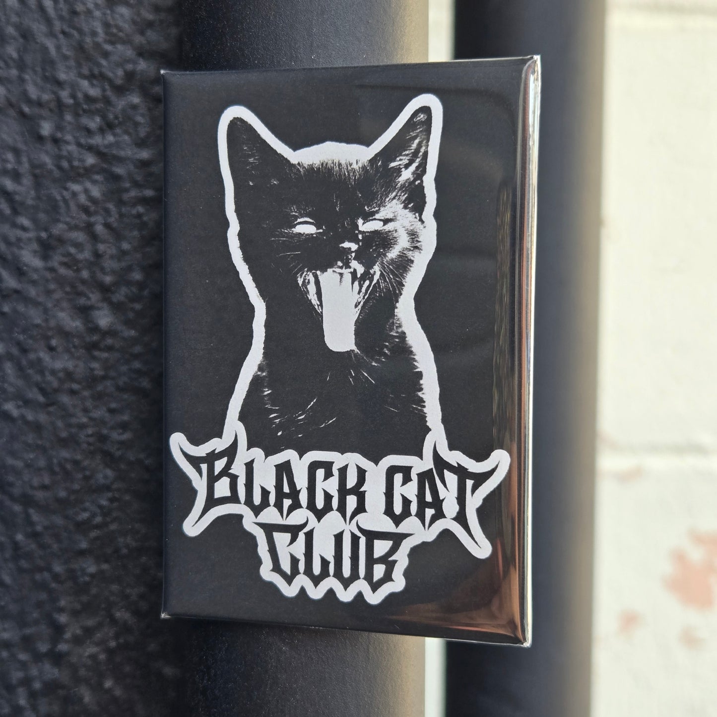A fridge magnet featuring a white silhouette of a hissing kitten with the text 'Black Cat Club'