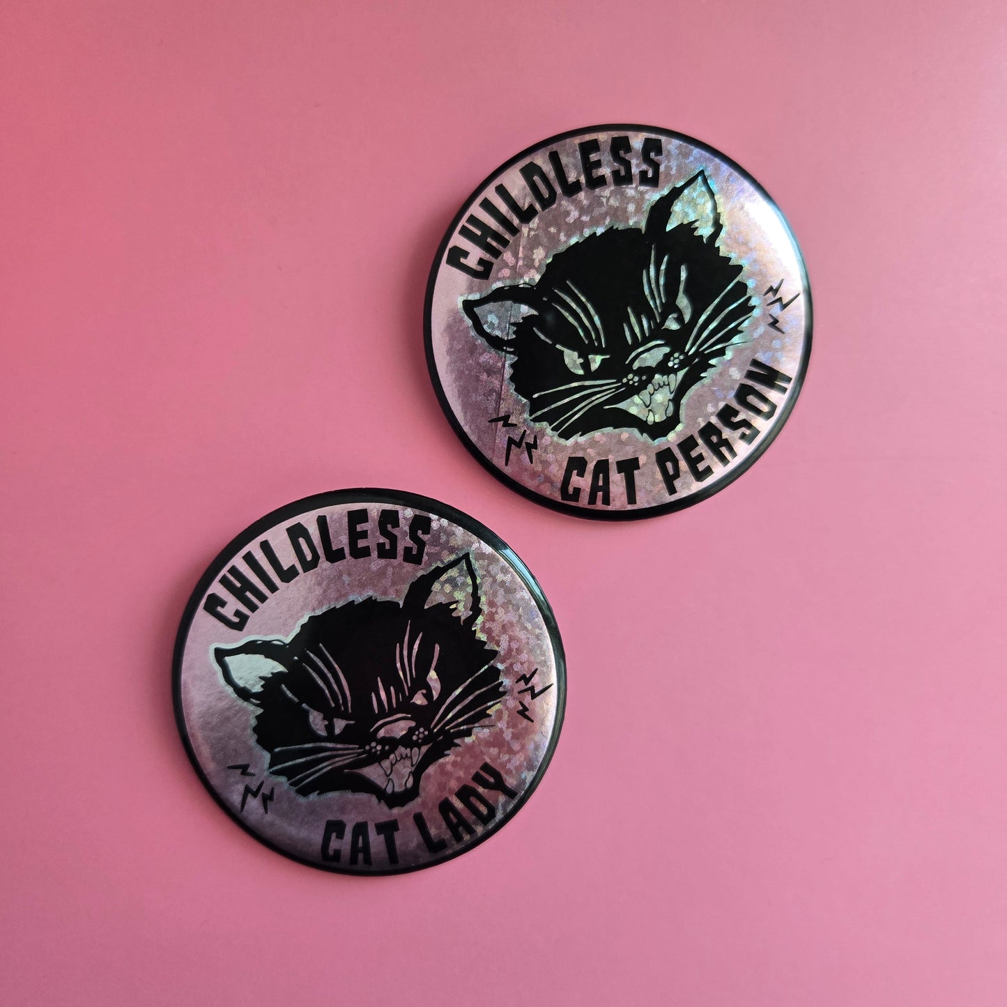 2 round buttons one with text 'Childless Cat Person' and one with text 'Childless Cat Lady' on a pink sparkle background, featuring a black cat.