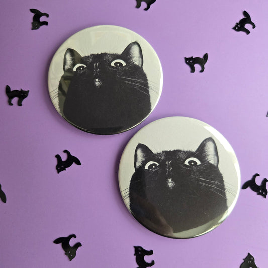 Two circular magnets with a silly black cat photo, displayed on a purple background with small black cat confetti.