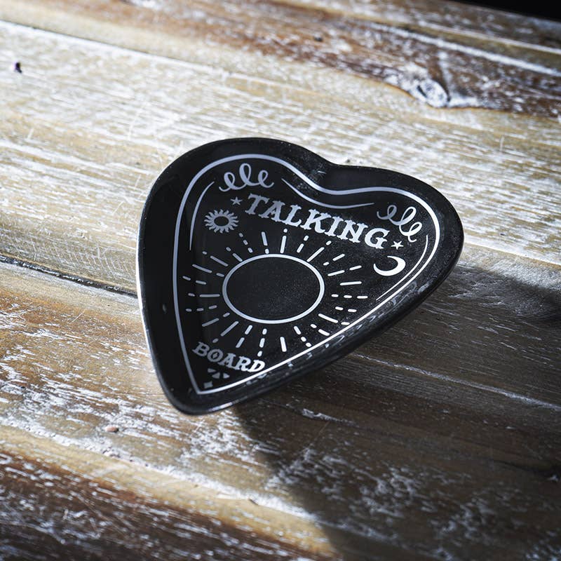 A black ceramic trinket dish in the shape of a planchette with 'TALKING BOARD' text and sun and moon motifs.