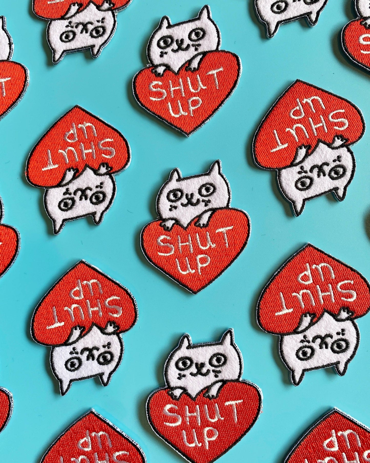 Pattern of cat-themed patches with 'SHUT UP' text on red hearts against a blue background.