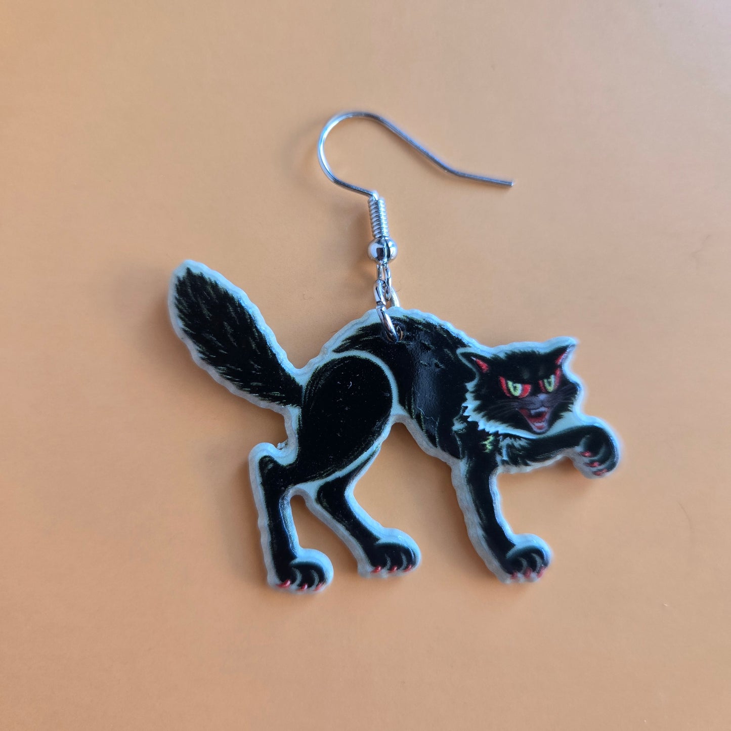 Black cat-shaped earring on a pale orange background