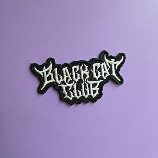 Black and white embroidered patch of the Black Cat Club logo on a purple background