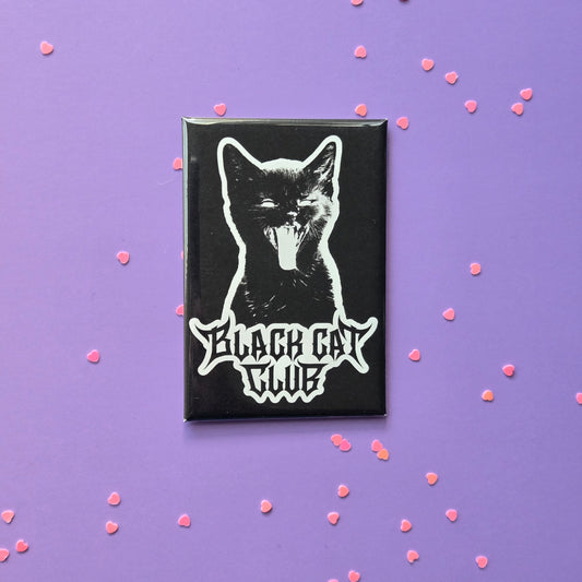 A fridge magnet featuring a white silhouette of a hissing kitten with the text 'Black Cat Club' on a purple background, surrounded by small pink heart-shaped decorations.