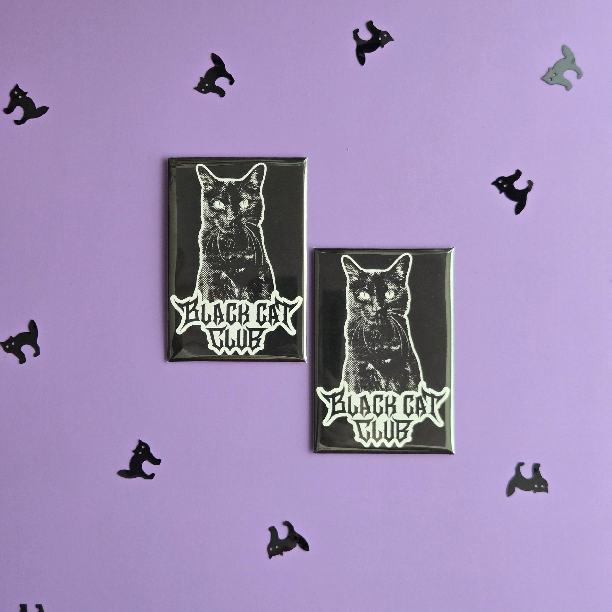 Two black rectangular magnets with a black cat illustration and Black Cat Club logo, displayed on a purple background with small black cat confetti.