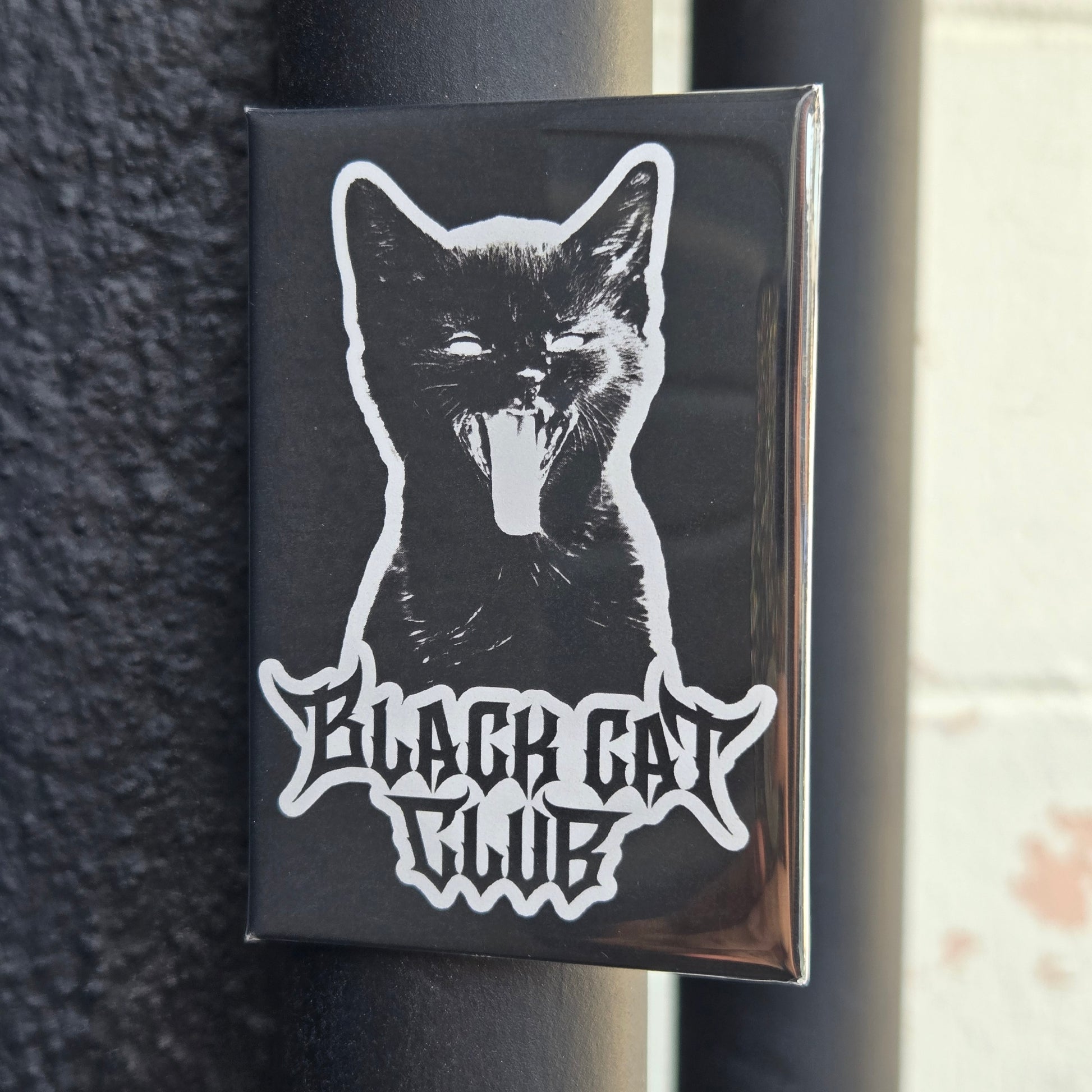 A fridge magnet featuring a white silhouette of a hissing kitten with the text 'Black Cat Club' 