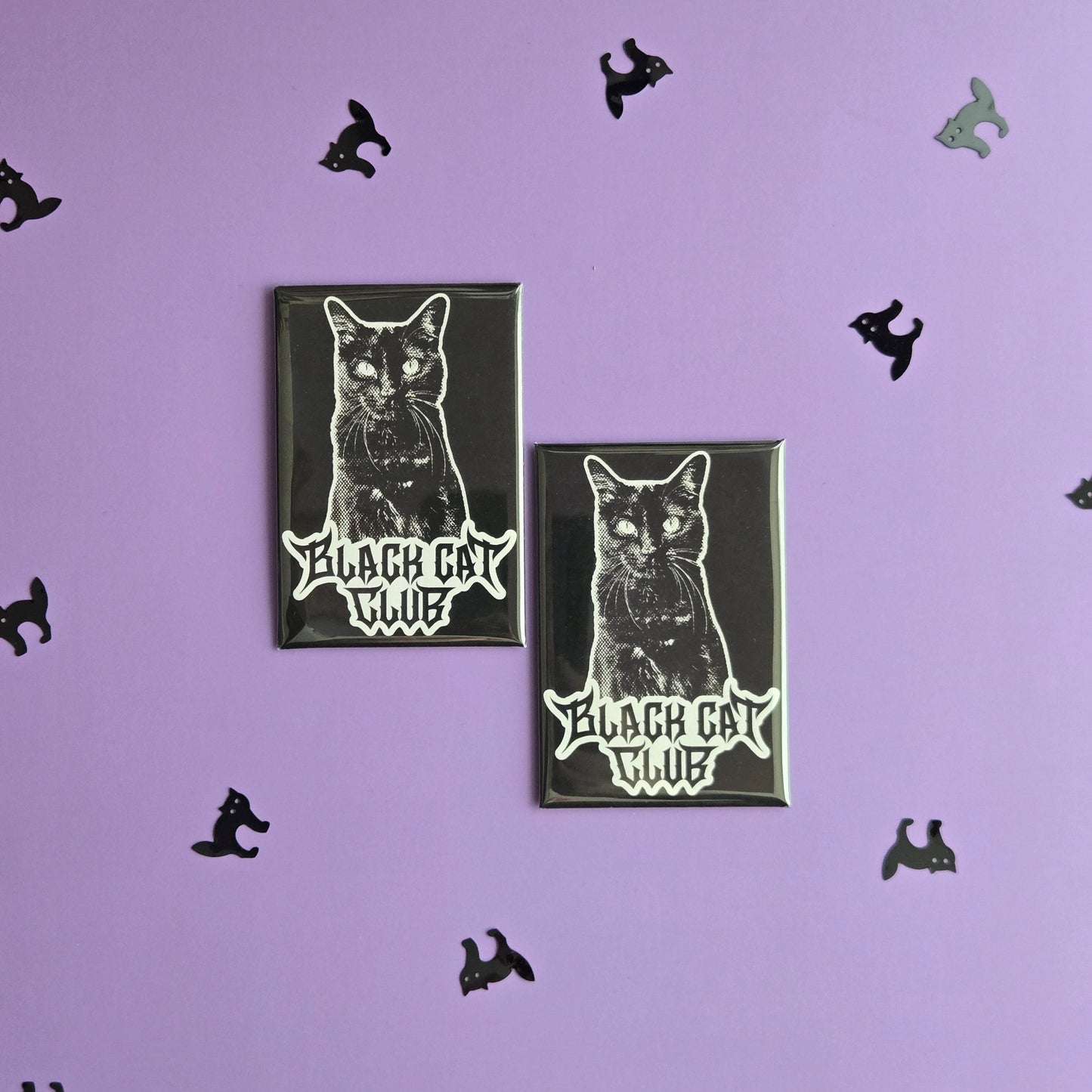 Two black rectangular magnets with a black cat illustration and Black Cat Club logo, displayed on a purple background with small black cat confetti.