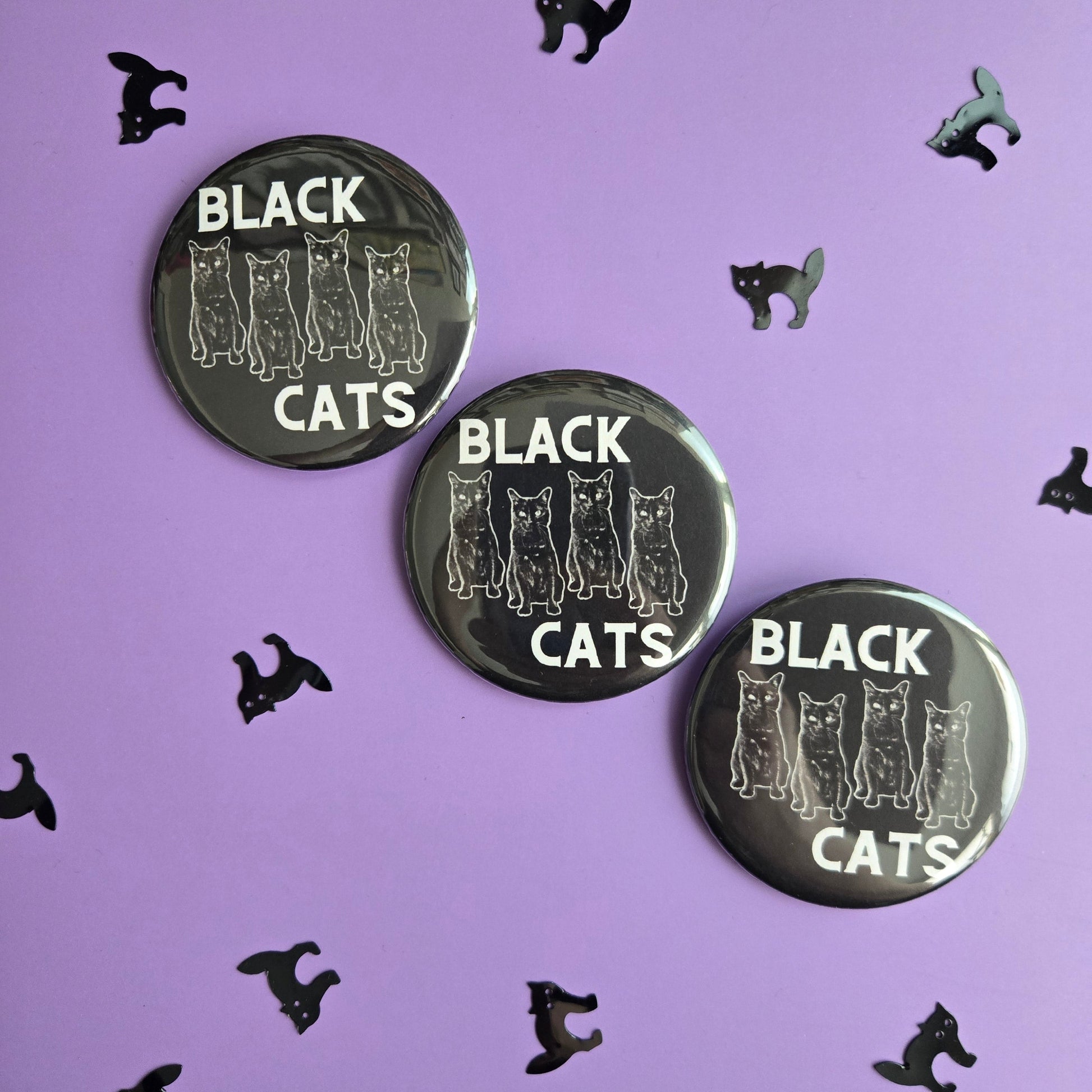 Black 'BLACK CATS' buttons, displayed on a purple background with black cat confetti.