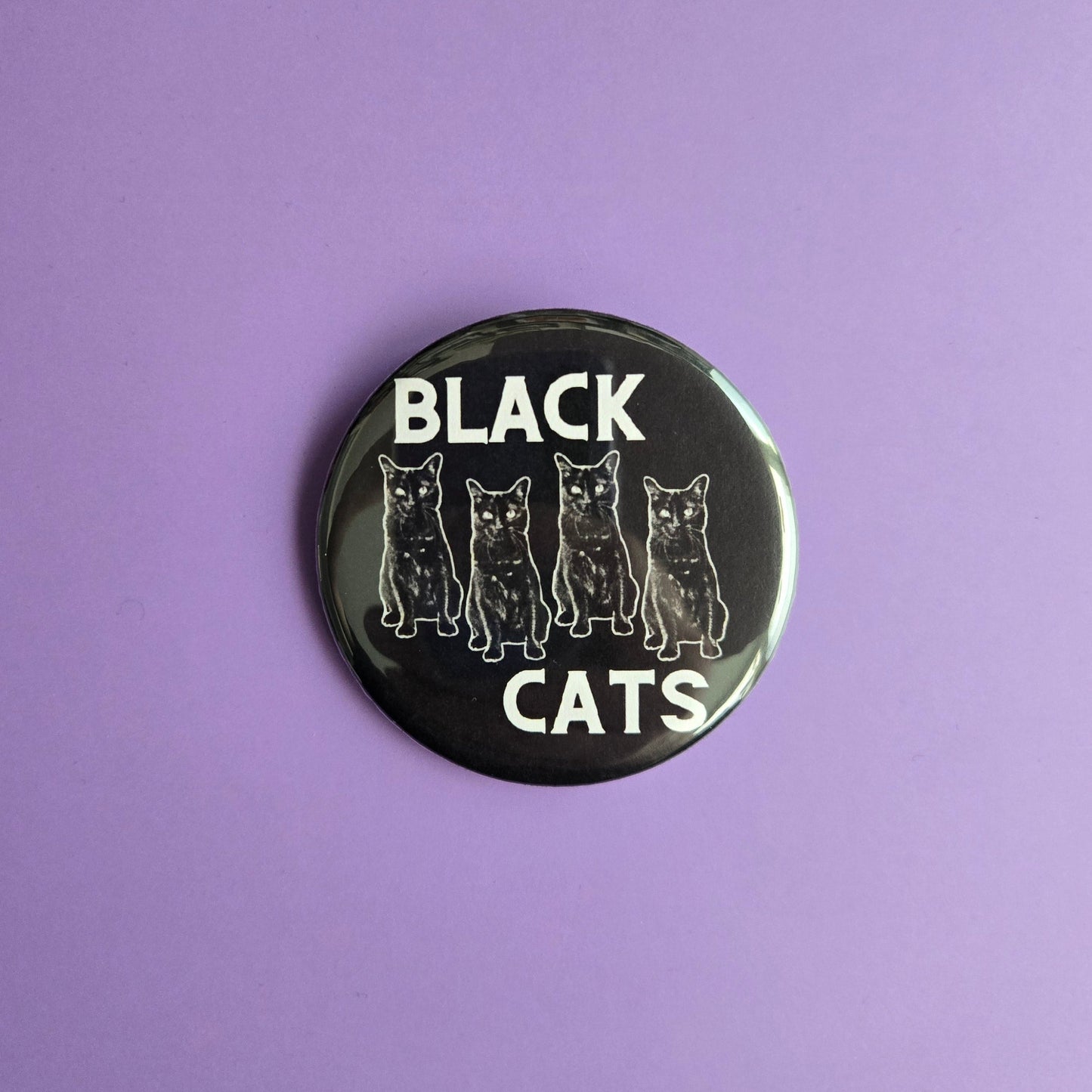 Button badge with 'Black Cats' text displayed on a purple background with cat confetti on a purple background
