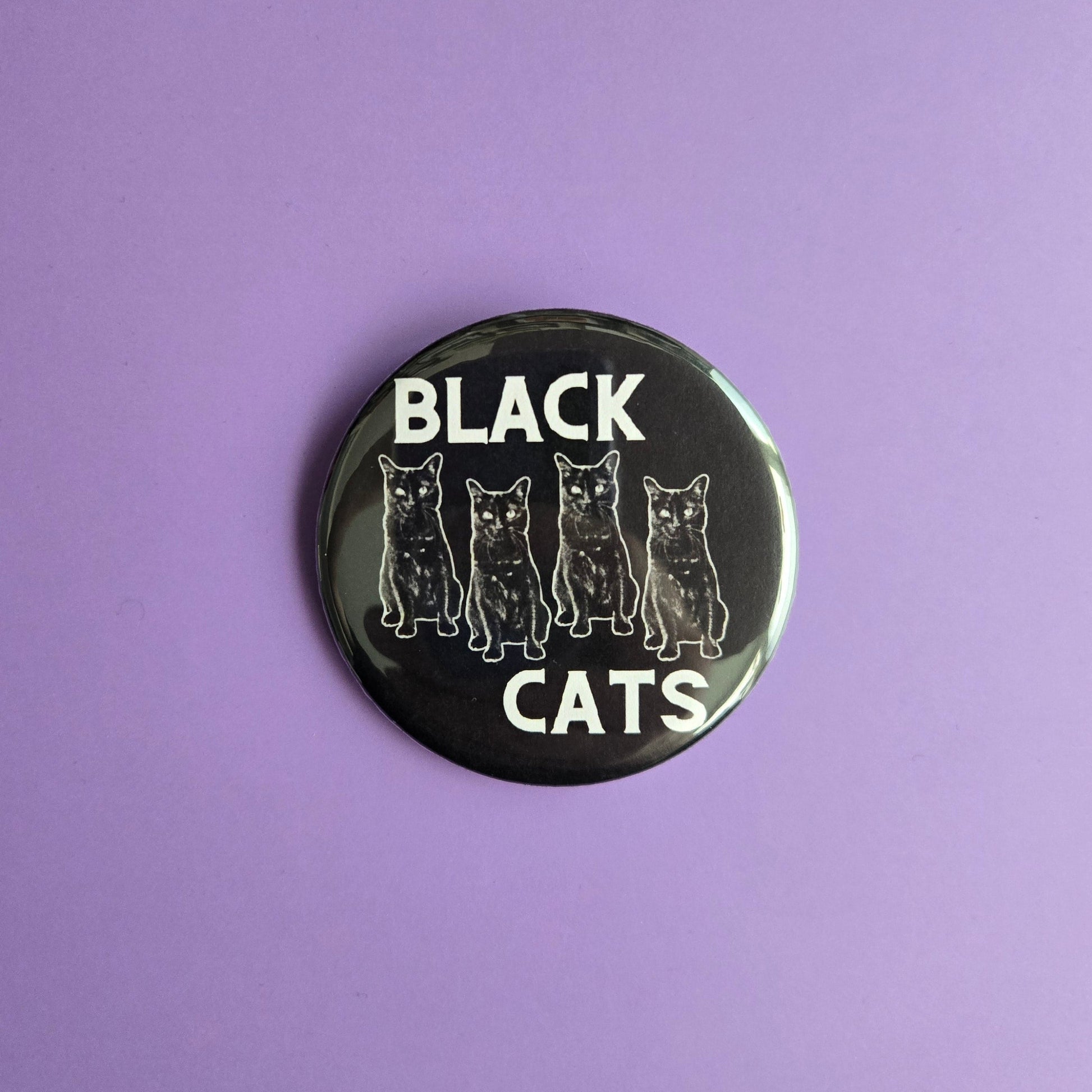 Button badge with 'Black Cats' text displayed on a purple background with cat confetti on a purple background