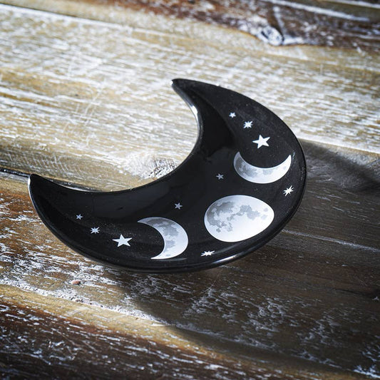 Black crescent moon-shaped dish with white moon phases and stars on a wooden surface