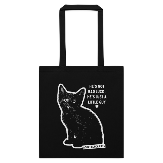 A black canvas tote bag with a white graphic of a sitting black cat and the text 'HE'S NOT BAD LUCK, HE'S JUST A LITTLE GUY' and 'ADOPT BLACK CATS'.