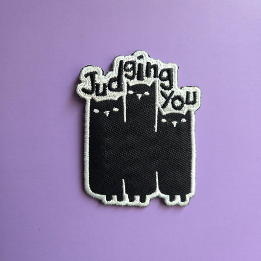 Black and white patch that reads Judging You with 3 illustrated cats, on a purple background
