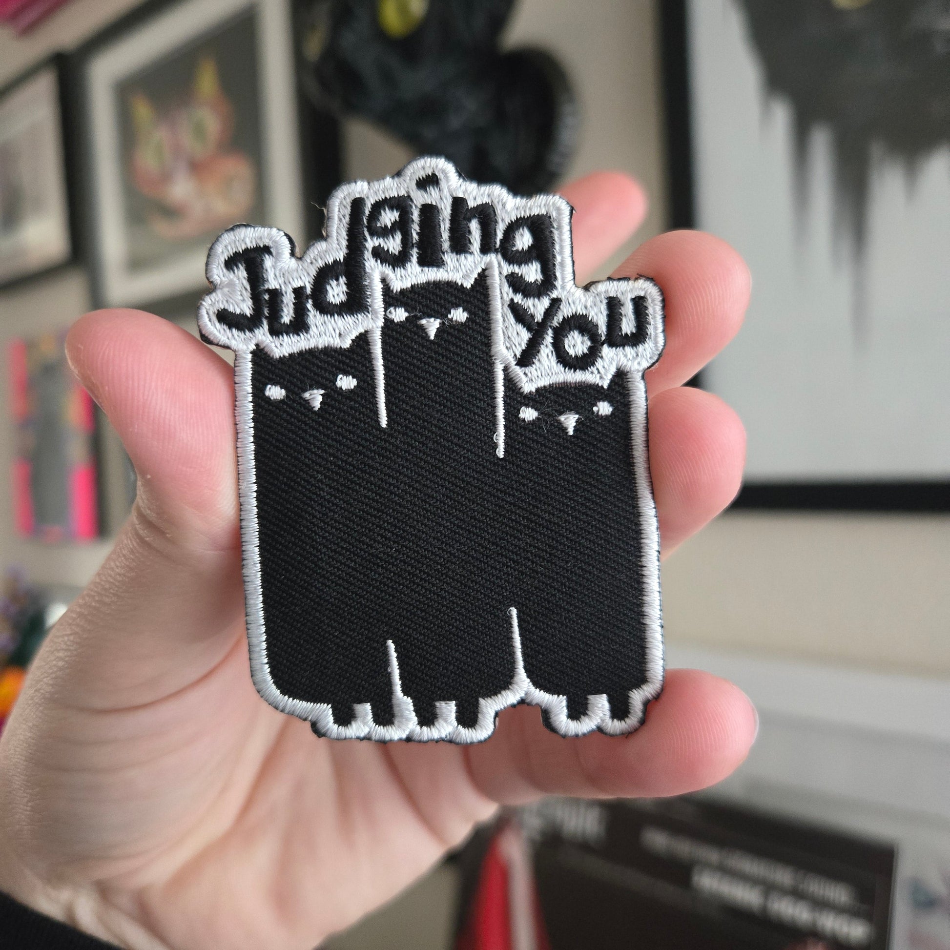 Hand holding a black and white patch with text against a blurred indoor background