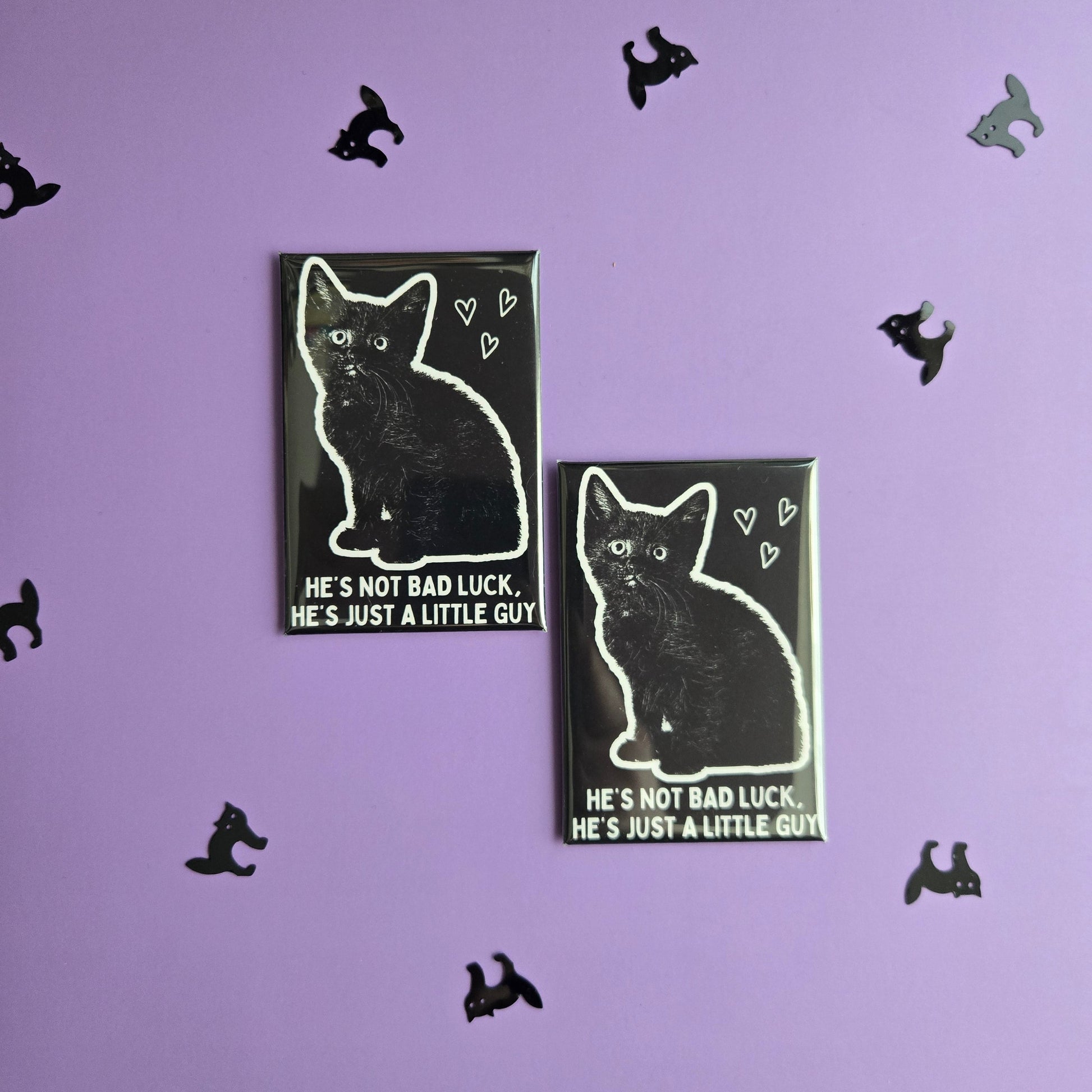 Two rectangular magnets with black and white cat illustrations reading 'He's not bad luck he's just a little guy' displayed on purple background.