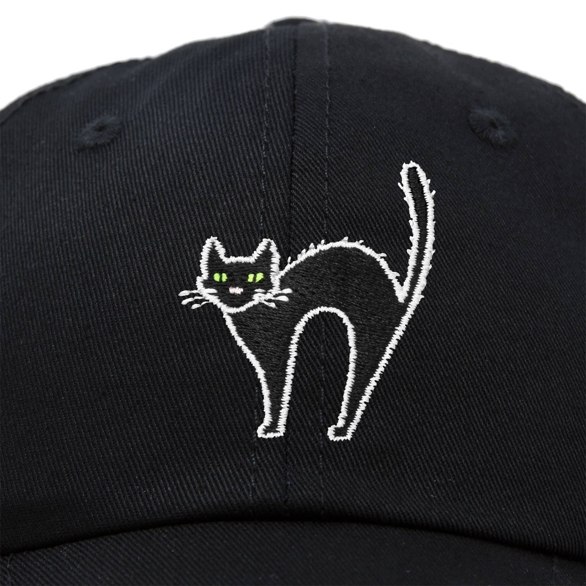 Black baseball cap with a white embroidered design of a cat with arched back and green eyes.