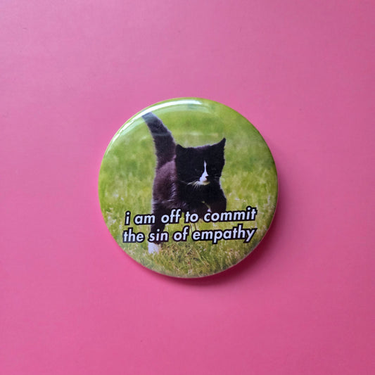 Button with an image of a black cat on a grassy background and the text 'i am off to commit the sin of empathy'.