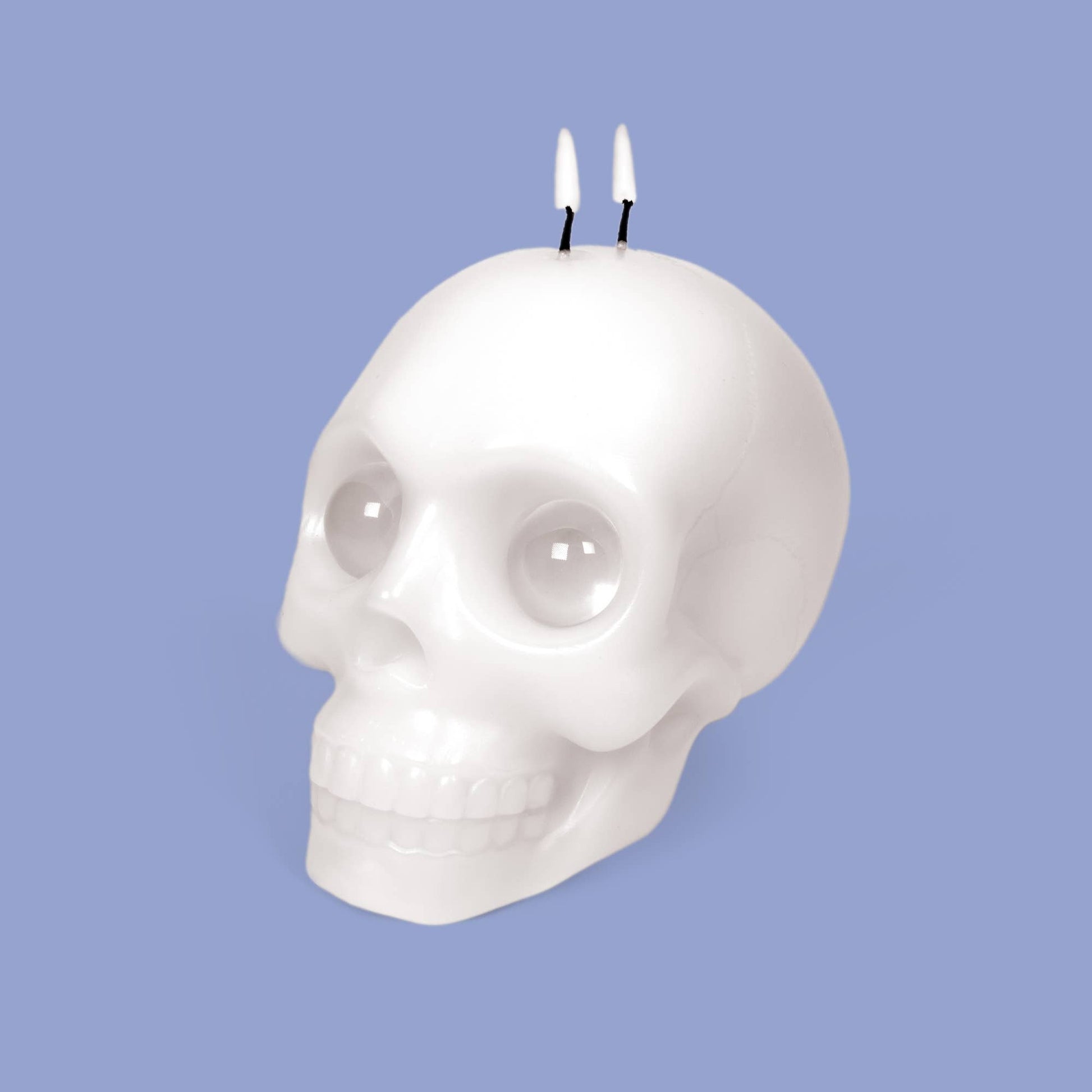 Skull-shaped candle with two wicks on a light purple background