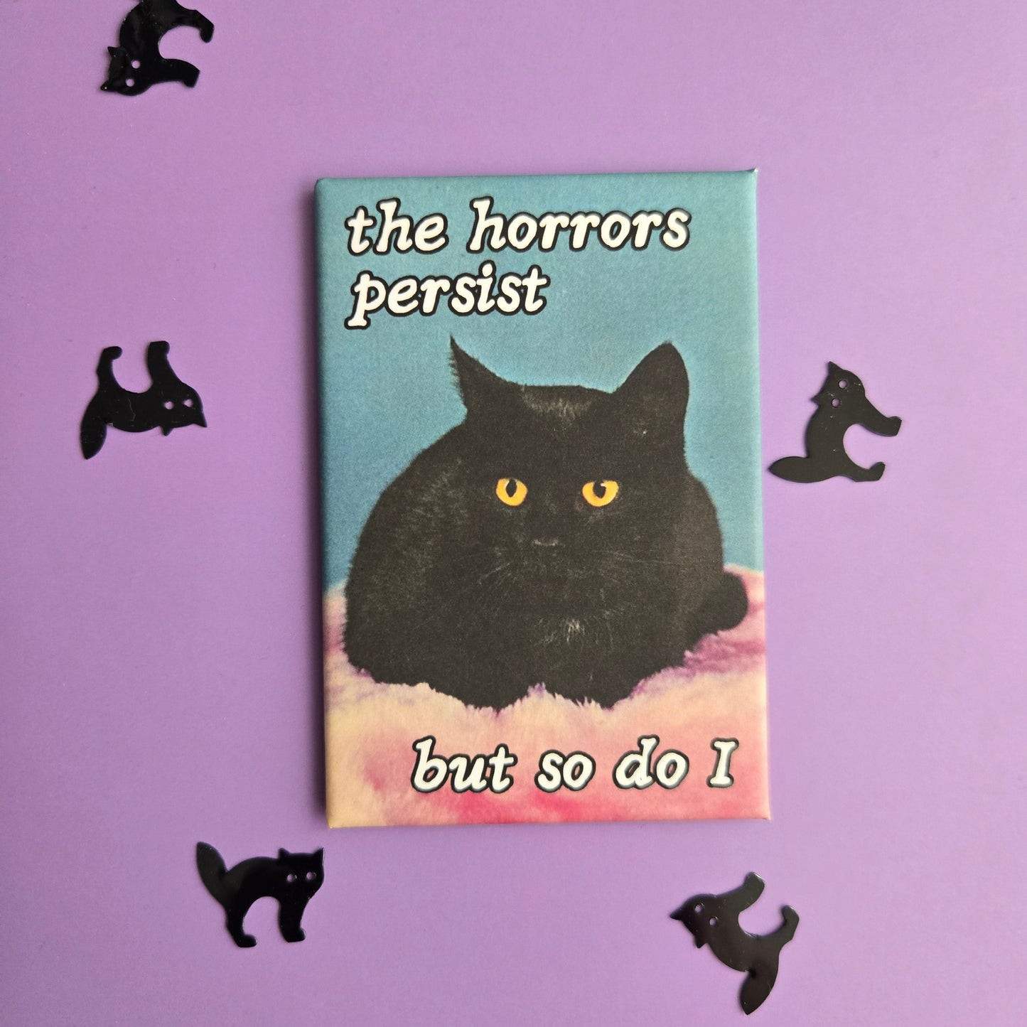 Rectangular magnet with vintage black cat photo and text reading The Horrors Persist But so Do I displayed on a purple background with black cat confetti.