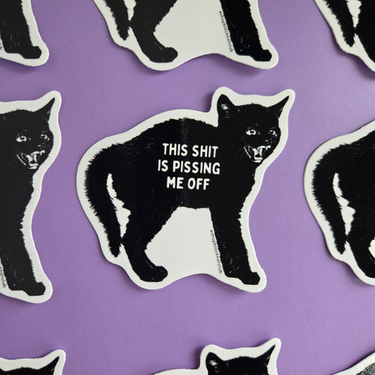 A sticker with a black cat design and the text 'This Shit Is Pissing Me Off' on a purple background.