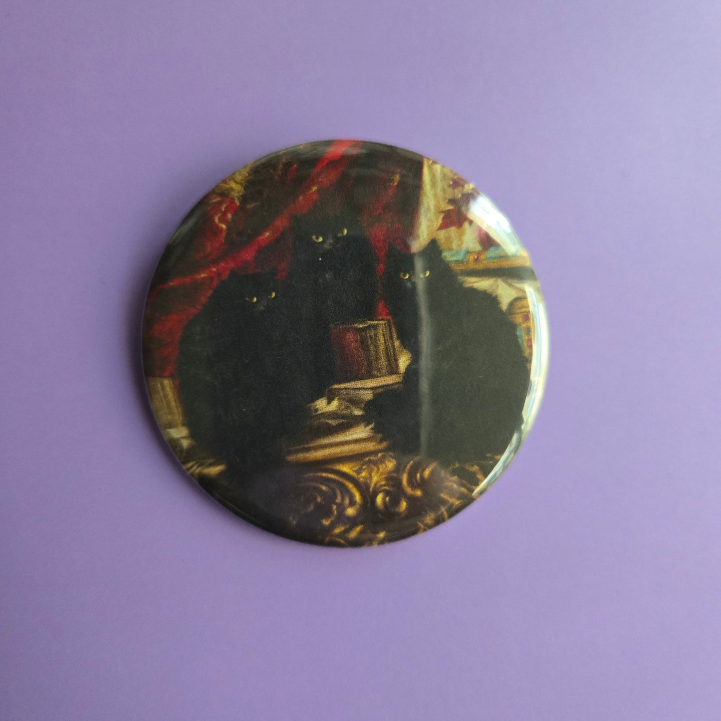 Round button with decorative with intricate design of Carl Kahler's painting '3 black cats', on a purple background