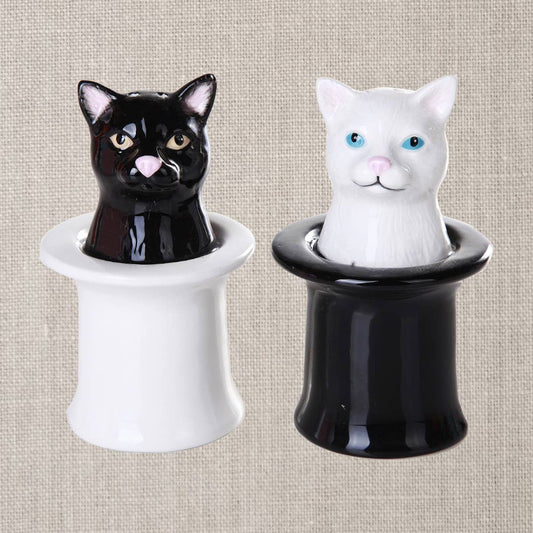 Two ceramic cat salt and pepper shakers, one black and one white, on a textured beige background.
